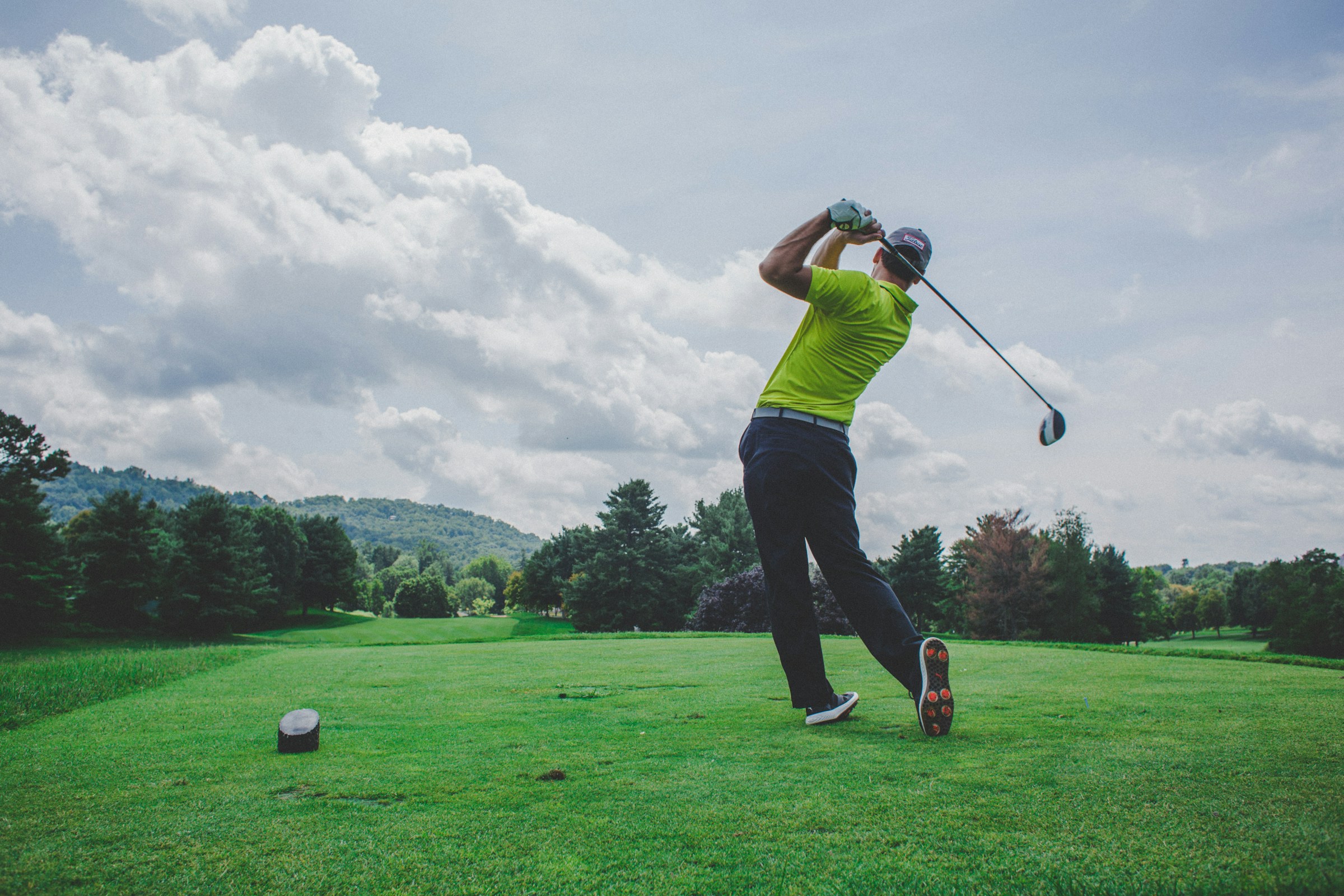 A golfer following through on a drive across a sunlit fairway